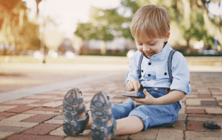 Smartphone. Bub sitzt am Boden und betrachtet ein Smartphone.